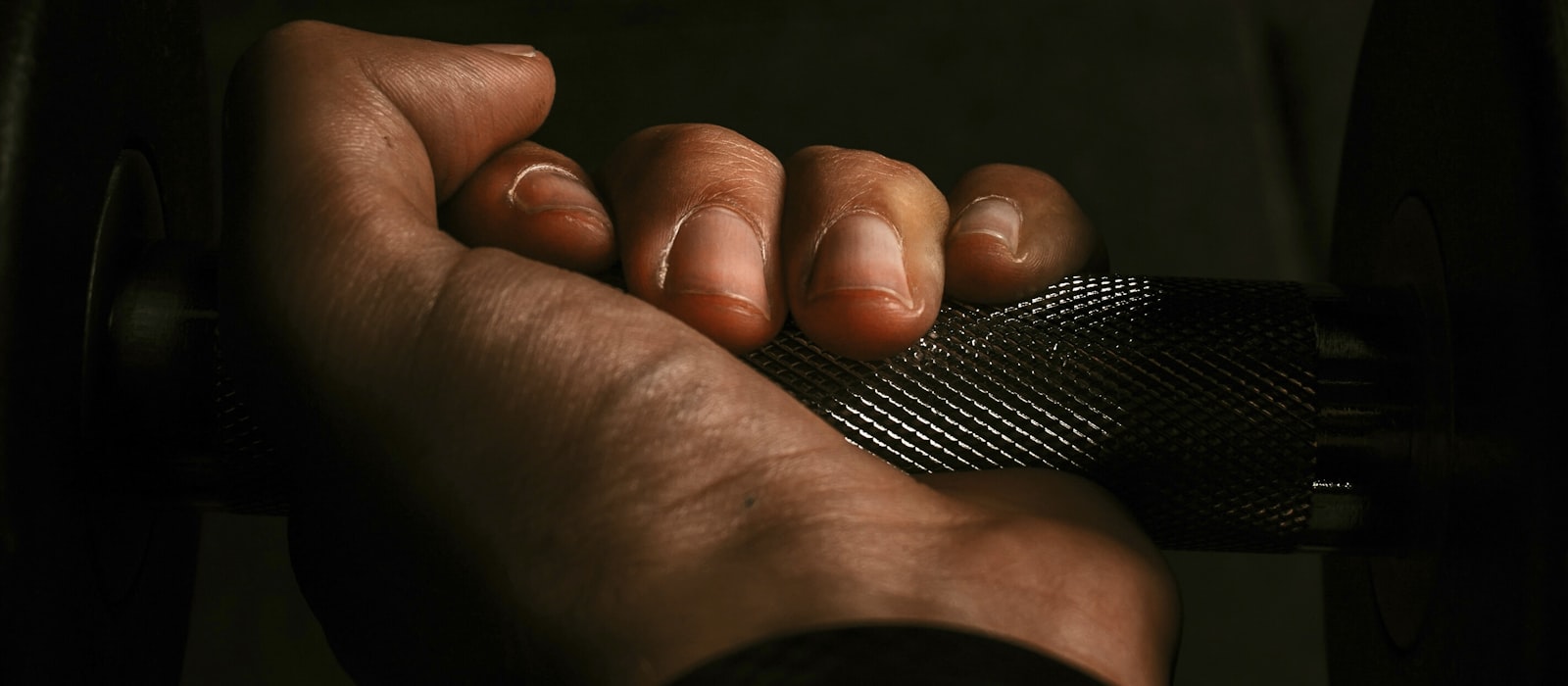 A bare hand gripping a knurled bar in the gym