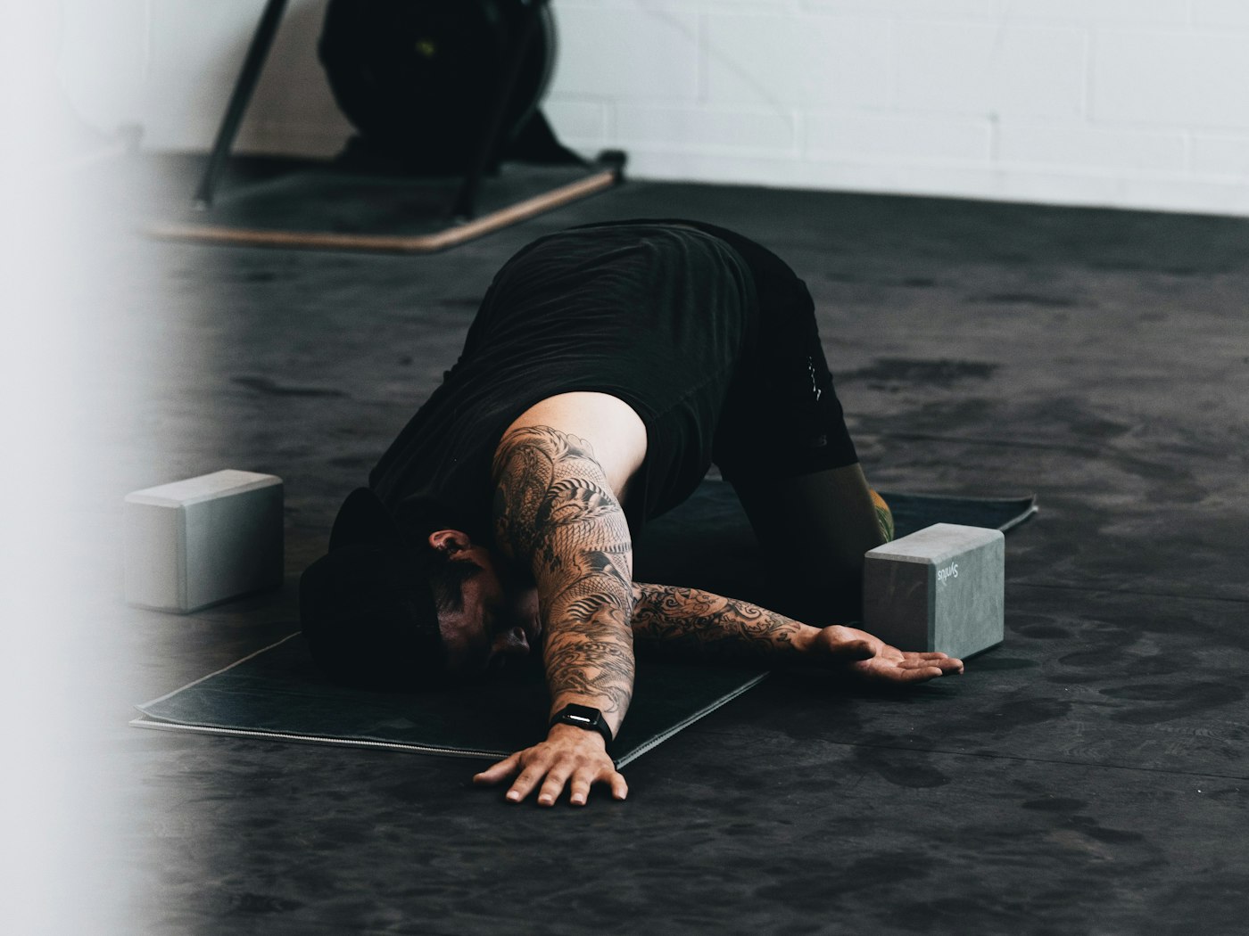 A member in an extended floor stretch on a black gym mat
