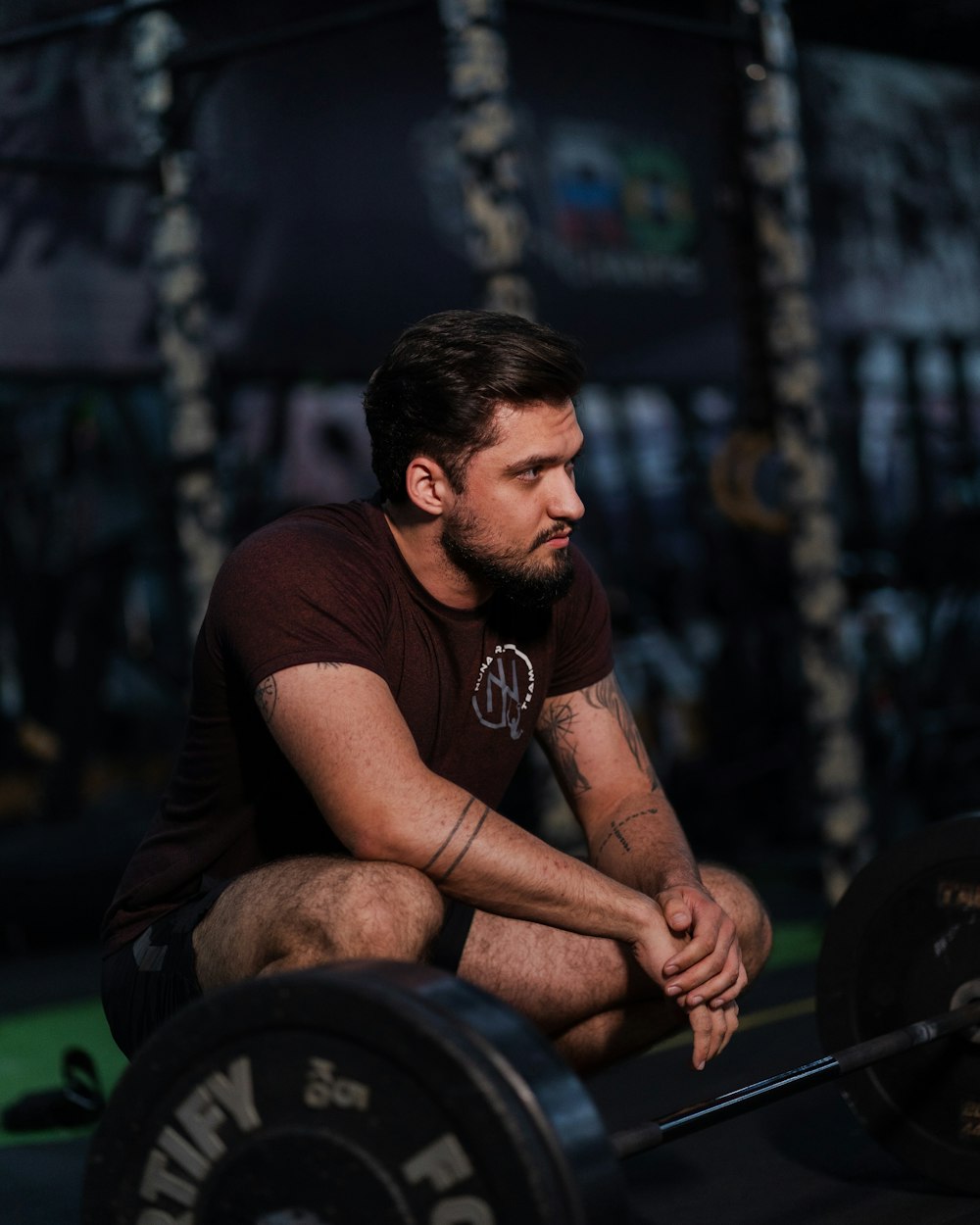 Ren Calder crouching at rest beside a loaded bar on the gym floor